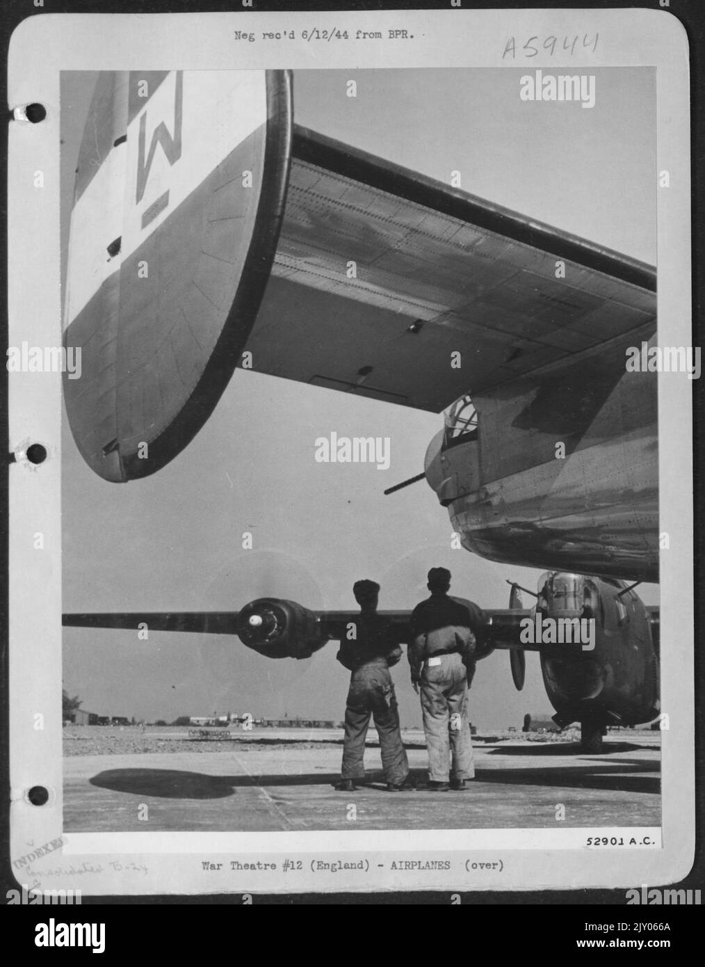 Zwei Bodencrewmen an einer konsolidierten B-24-Station sind unter dem fotogenen Liberator-Heck eingerahmt, als sie eine Minute lang die Arbeit in ihrem Flugzeug stoppten, um zu beobachten, wie die Motoren in der nächsten Neugestaltung auf dem Liberator 'aufgetrieben' wurden, was alle dazu führte Stockfoto