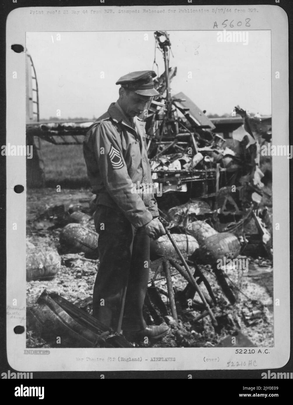 M/Sgt. George Clevanik aus Irwin, Pennsylvania, inmitten der übersäten Trümmer des konsolidierten Liberators „Vadie Raye“ aus dem Jahr B24, auf dem er Ingenieur und Schütze war, zeigt auf, wo er vom Laufsteg aufgehängt und als loderndes Schiff auf der Landebahn entlang geschleppt wurde Stockfoto