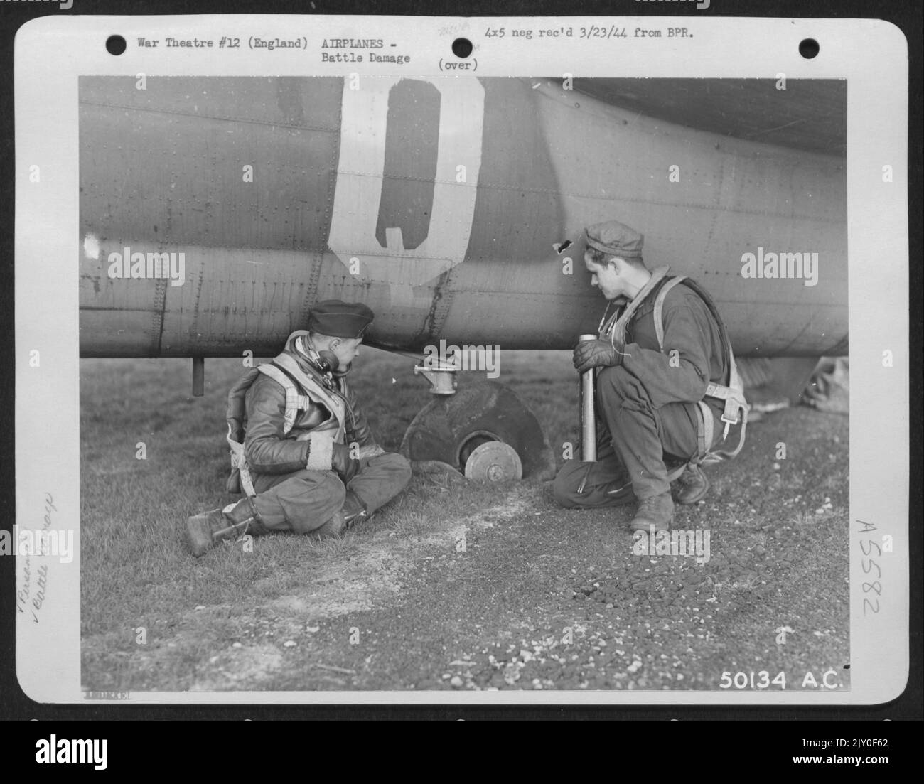 ENGLAND-Flak durchbohrt den Hinterradreifen über Berlin, verhinderte aber nicht, dass der Pilot eine gute Landung auf der Heimatbasis machte. Gezeigt, die das Rad untersuchen, sind 2. LT. Homer Glass, Chicago (links) und Sgt. Megchelsen, Ainsworth, Iowa. Ein Flakloch im Rumpf kann sein Stockfoto