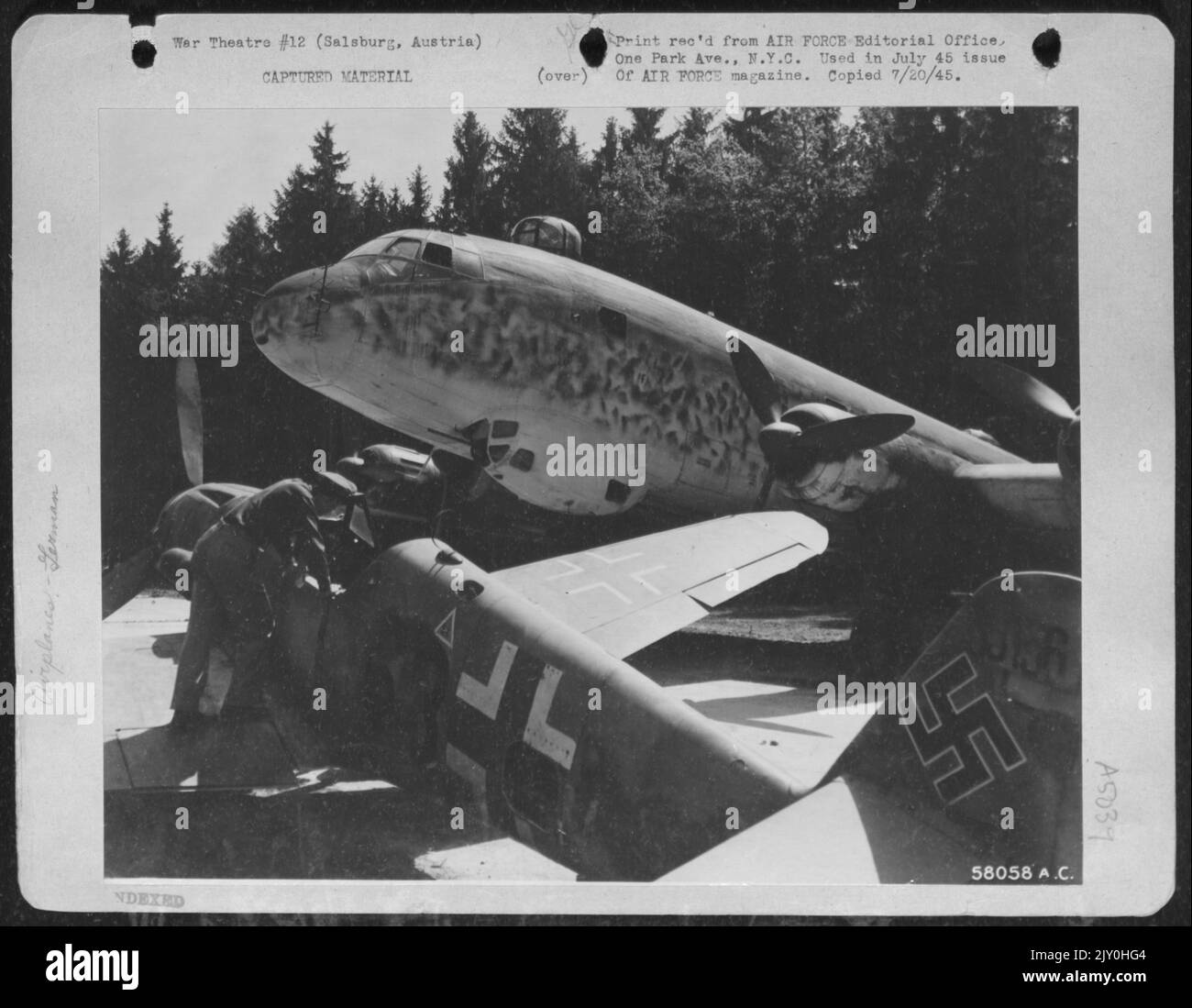 Ein amerikanischer Pilot inspiziert Eine Me-109 auf dem Hitlerfeld in Salsburg, Österreich. Im Hintergrund steht eine Focke-Wulf FW-200, ein riesiger Transport, wahrscheinlich Hitlers Flugzeug. Stockfoto