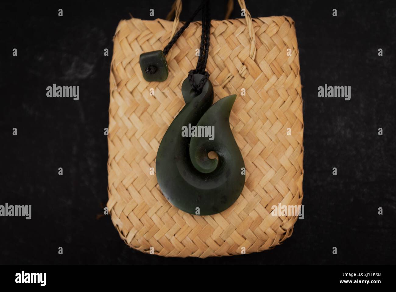 Pounamu Fischhaken Halskette auf gewebten Flachs Tasche auf dunklem Hintergrund. Aotearoa, Neuseeland, Maori. Stockfoto