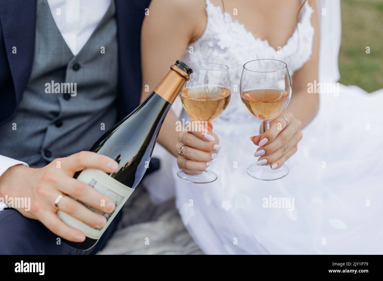 Nahaufnahme aus der Hand des Bräutigams und der Braut, die aus der Flasche und aus den Gläsern Sekt trinken und gießen Stockfoto