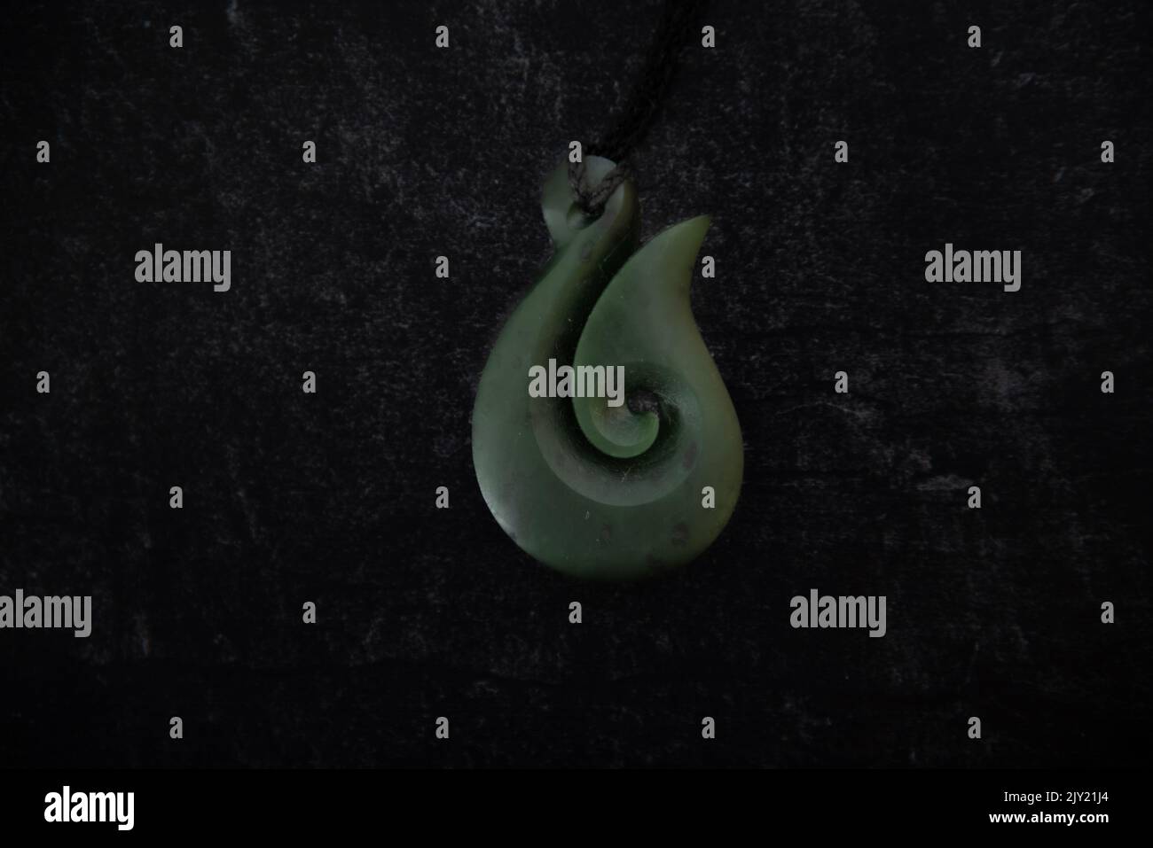 Pounamu Fischhaken Halskette auf dunklem Hintergrund. Aotearoa, Neuseeland, Maori. Stockfoto