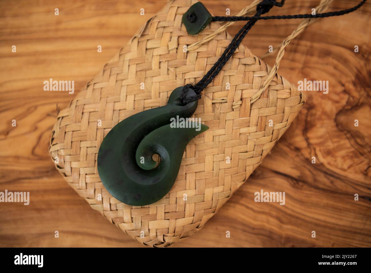 Pounamu Fischhaken Halskette auf körnigem Holzhintergrund. Aotearoa, Neuseeland, Maori. Seitenwinkelansicht. Stockfoto