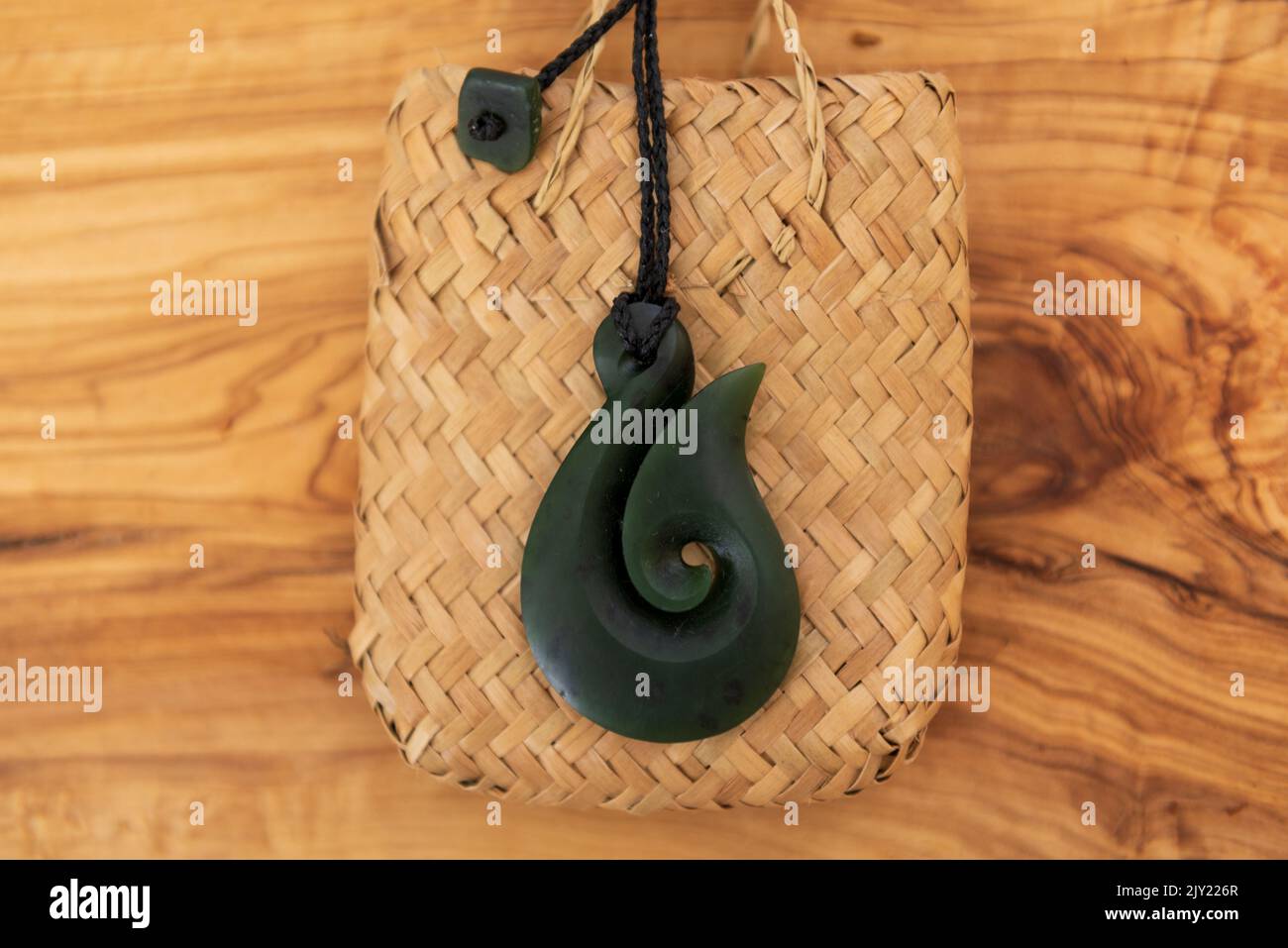 Pounamu Fischhaken Halskette auf körnigem Holzhintergrund. Aotearoa, Neuseeland, Maori. Draufsicht. Stockfoto