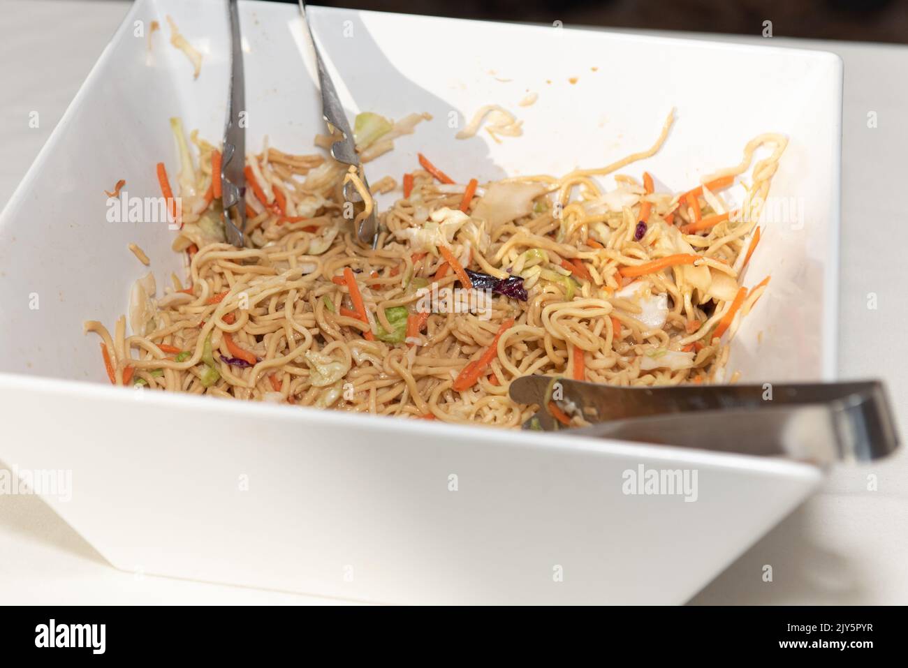 Eine Schüssel Nudelsalat hat zwei Zangen für die Gäste, um sich selbst das Essen zu essen zu servieren. Stockfoto