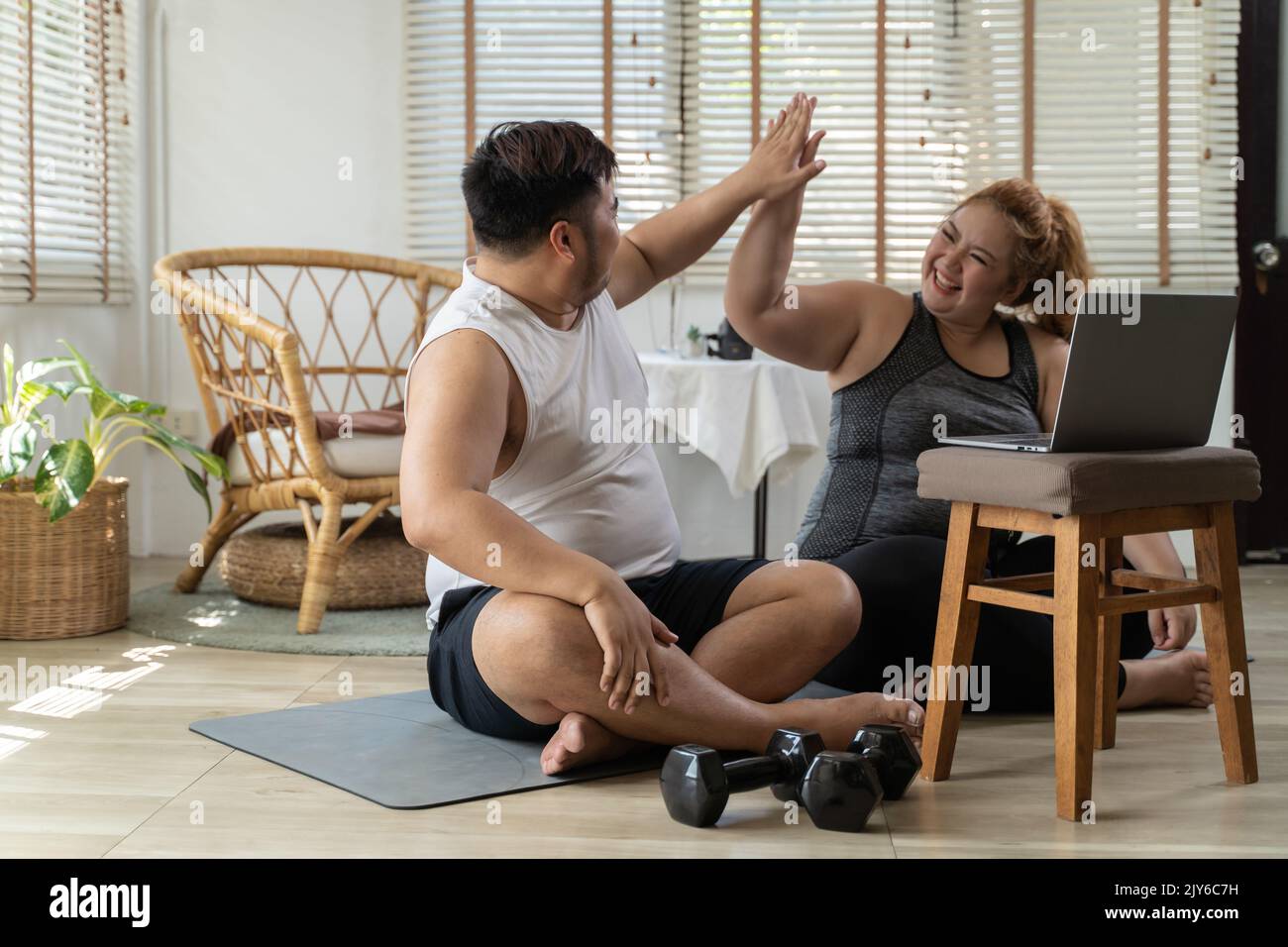 Junge asiatische mollige Paar trainieren und trainieren, während Sie sich ein Online-Training von Laptop zu Hause. Mann und Frau lächeln und tun hohe fünf Geste mit Partner drinnen. Stockfoto