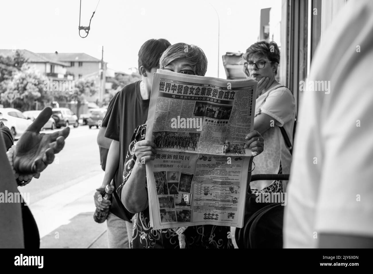 Frau liest chinesische Gemeinschaftszeitungen, während sie in einem Restaurant in Cabramatta, Sydney – New South Wales, Australien ansteht Stockfoto