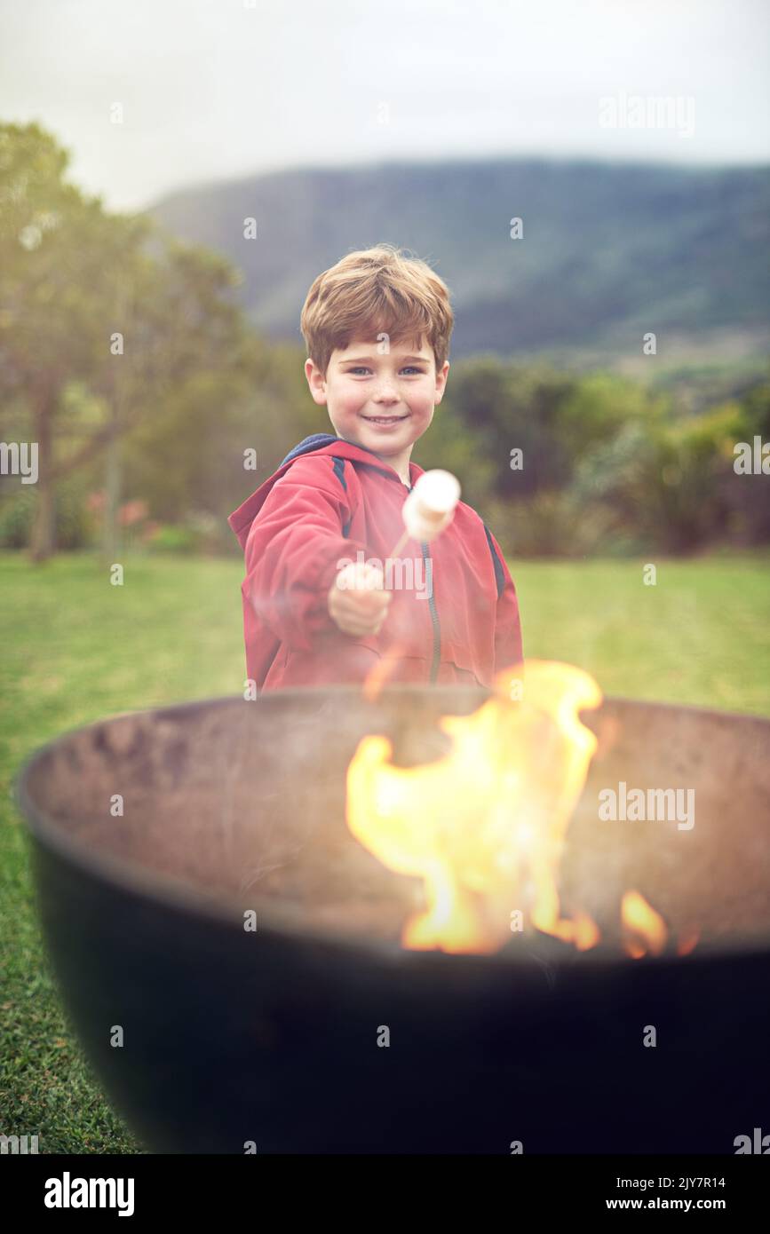 Geröstete Sumpfmarmelibe sind die besten. Porträt eines kleinen Jungen, der eine Marschmanne über einem Feuer röstet. Stockfoto