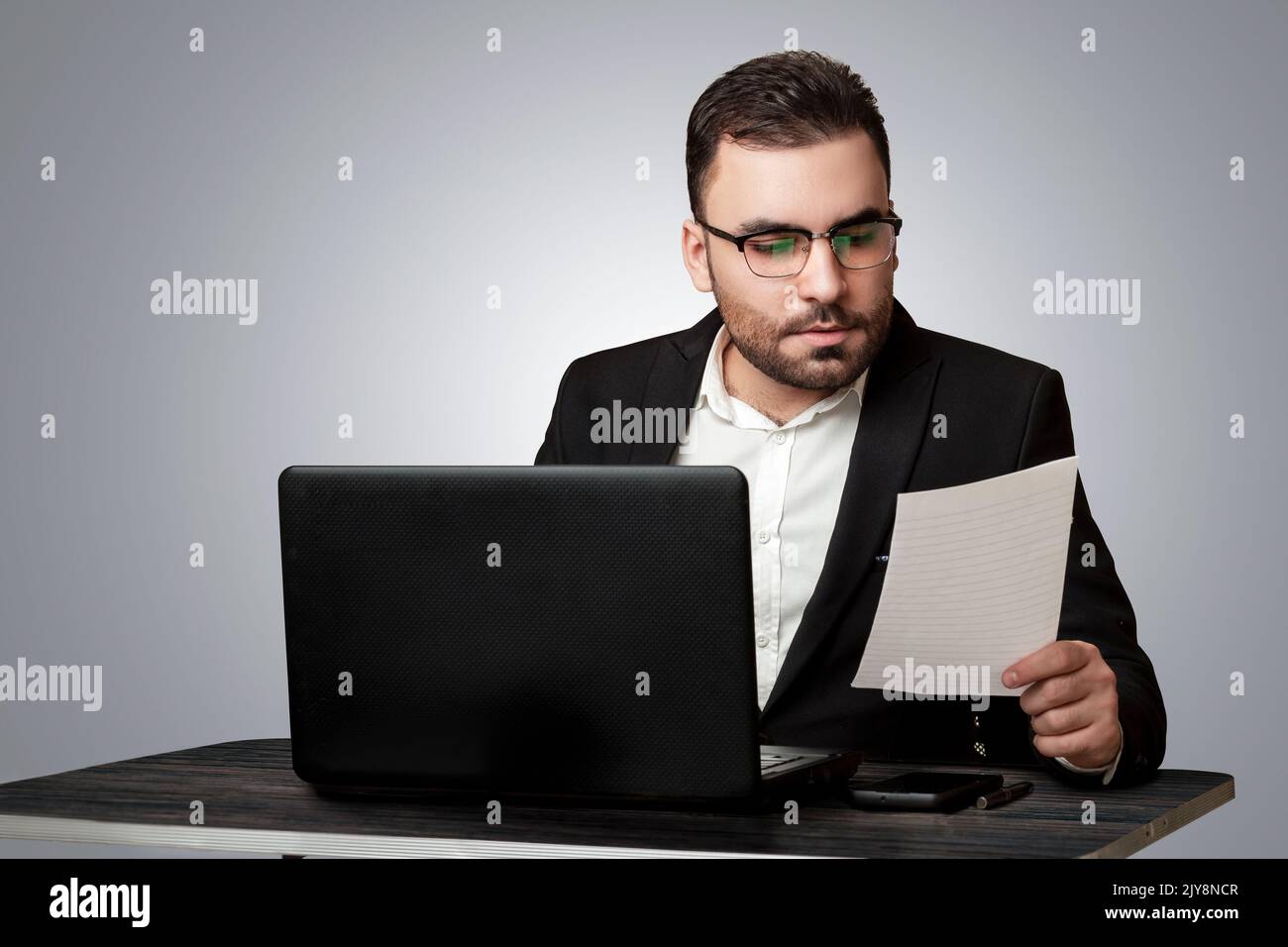 Ein hart arbeitender Mitarbeiter, der seine Arbeit an seinem Schreibtisch verrichtete, in einem formellen Anzug und einem abgeschiedenen Hintergrund gekleidet, Geschäftsmann Stockfoto