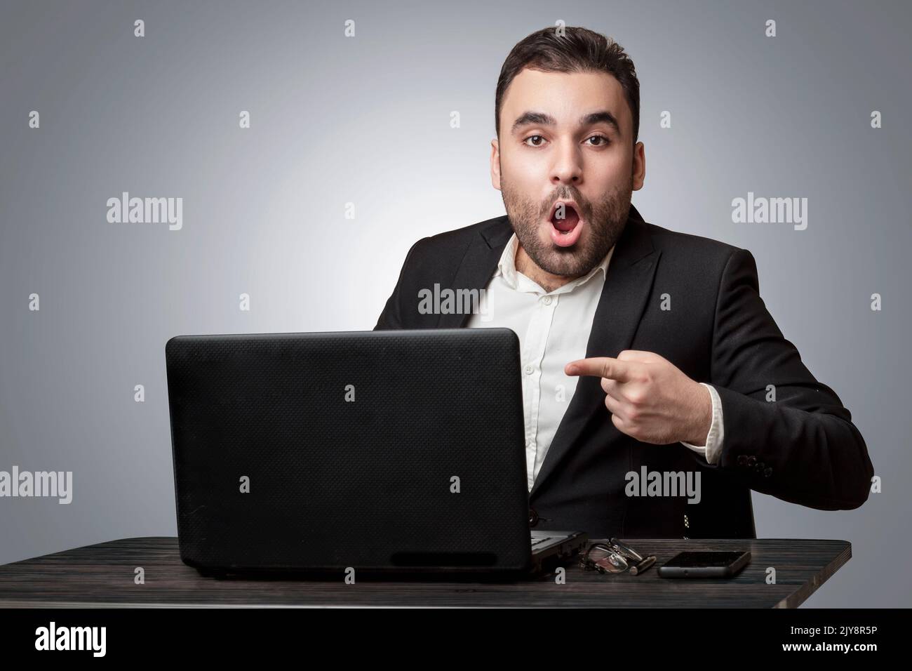 Überraschte Person, die hinter seinem Schreibtisch saß, auf den Laptop zeigte, isoliert, Hintergrund Stockfoto