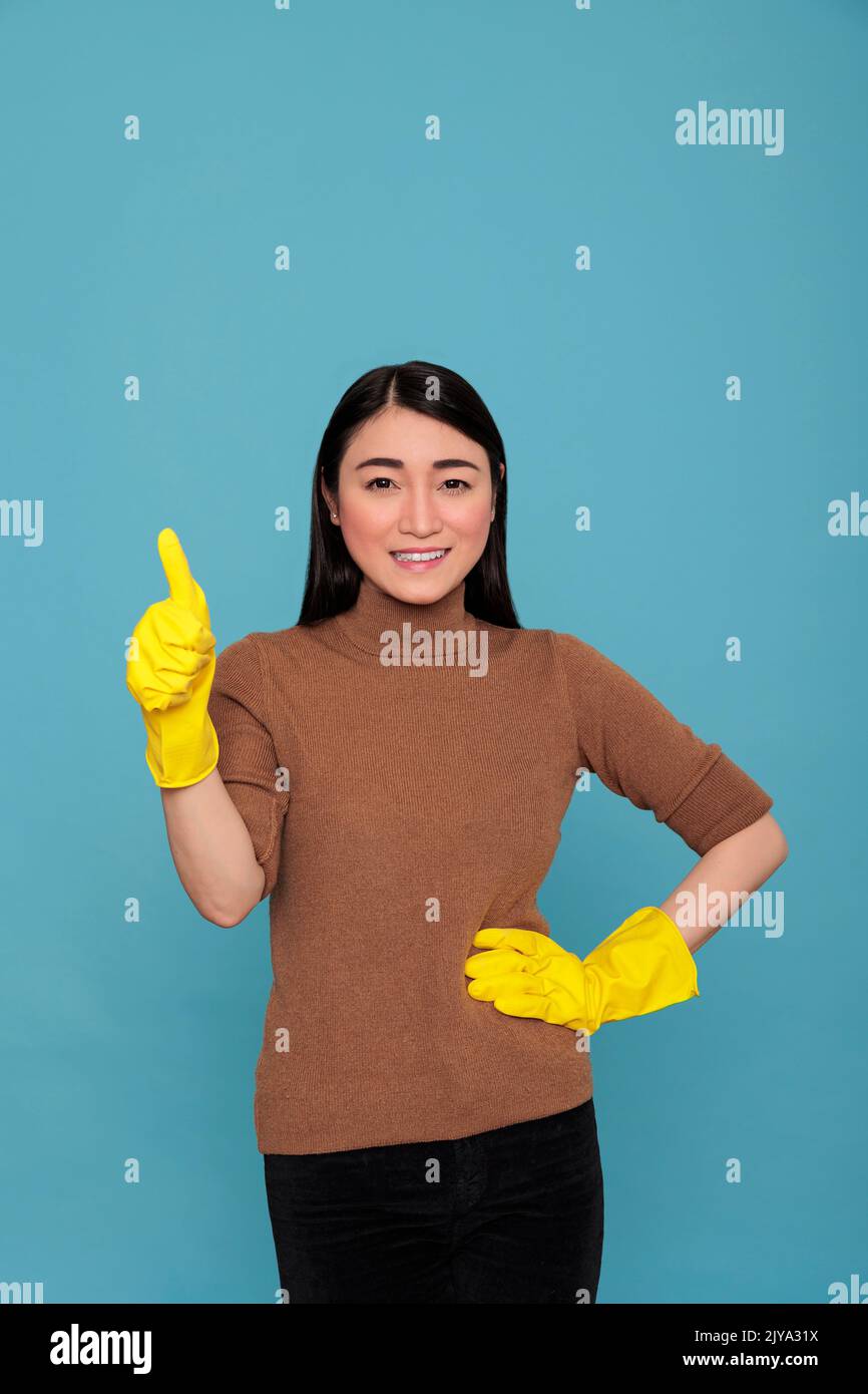 Asiatisch lächelnd glücklich asiatische Hausmädchen Daumen nach oben und tragen gelbe Handschuhe für die Handsicherheit, Reinigung Home Konzept, zufrieden lachen und positive Geisteszustand Frau bereit, Tag zu Tag Aufgaben zu tun Stockfoto