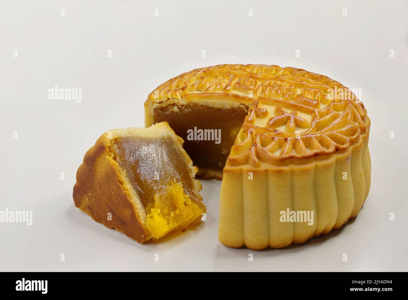 Gebackener chinesischer Mondkuchen mit Lotuskernpaste und geschnittenem Keil mit gesalzenem EntenEigelb auf weißem Hintergrund. Stockfoto