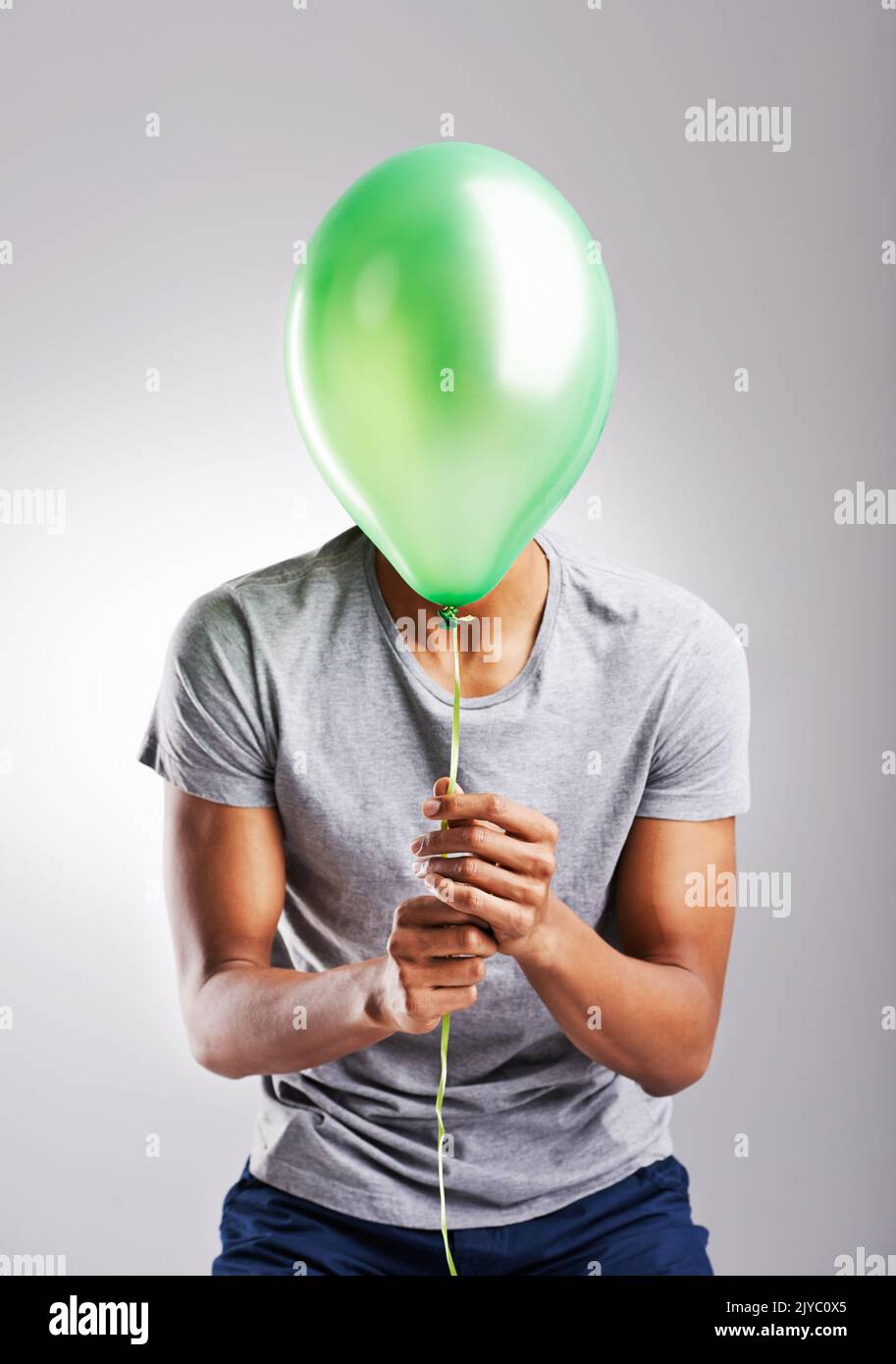 Lass los und lass dich frei. Ein Mann bedeckt sein Gesicht mit einem Ballon auf einem grauen Hintergrund. Stockfoto