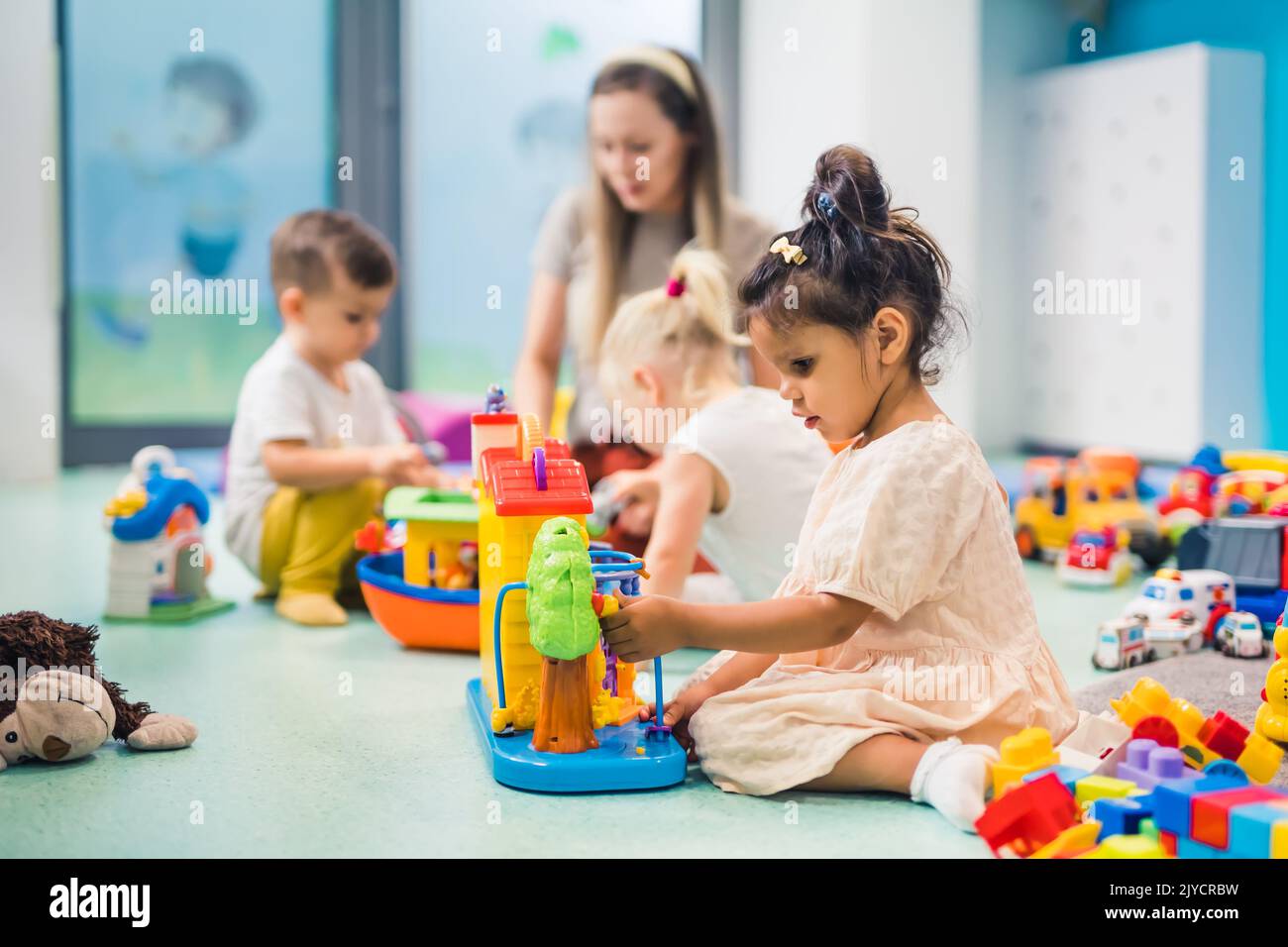 Kindergarten. Kleinkinder und ihre Lehrerin spielen mit bunten Plastikspielhäusern, Autos und Booten. Entwicklung von Phantasie, Kreativität, Feinmotorik und grobmotorischen Fähigkeiten. Hochwertige Fotos Stockfoto