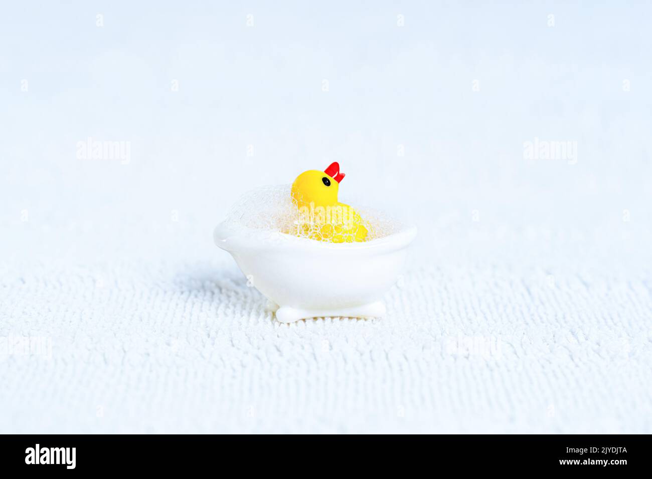 Bringen Sie die gelbe Ente in einer weißen Miniatur-Badewanne mit Seifenblasen zum Spielzeug. Kreatives Badekonzept. Stockfoto