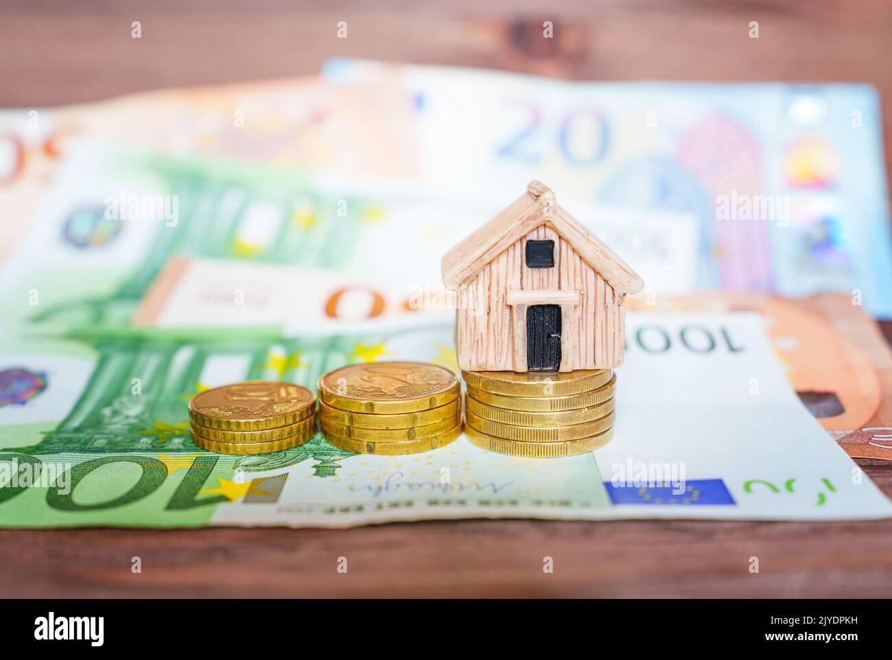 Miniaturhausmodell mit Münzstapeln und Euro-Banknoten auf einem Holztisch, selektiver Fokus. Home Loan-Konzept. Stockfoto