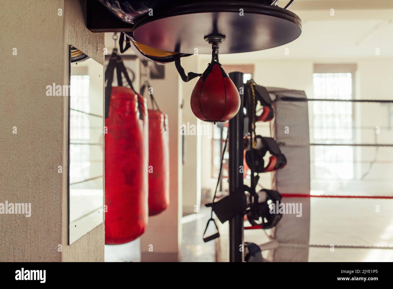 Kleiner roter Boxsack, der in der Nähe anderer Trainingsgeräte in einer Boxhalle hängt. Stillleben von einem Fitness-Studio während des Tages. Stockfoto