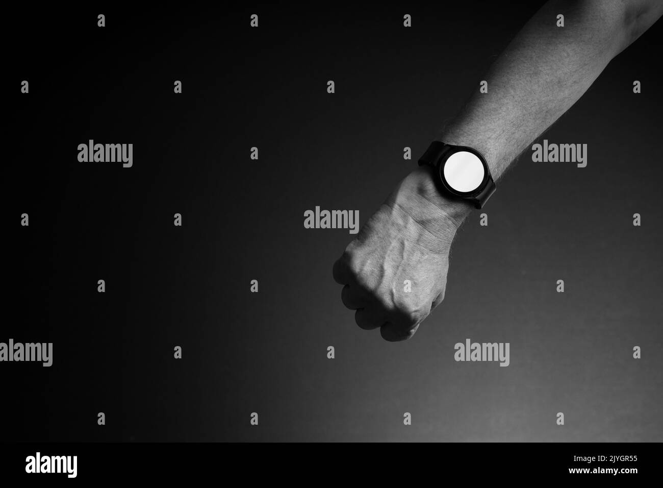 Schwarz-Weiß-Bild der Hand des Mannes mit Smart Watch am Handgelenk, Anzeige weißen leeren Bildschirm, isoliert auf dunklem Hintergrund mit Kopierraum Stockfoto