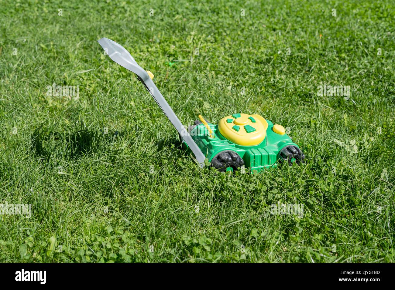 Kinderspielzeug-Rasenmäher auf ungeschnittenem Gras Stockfoto