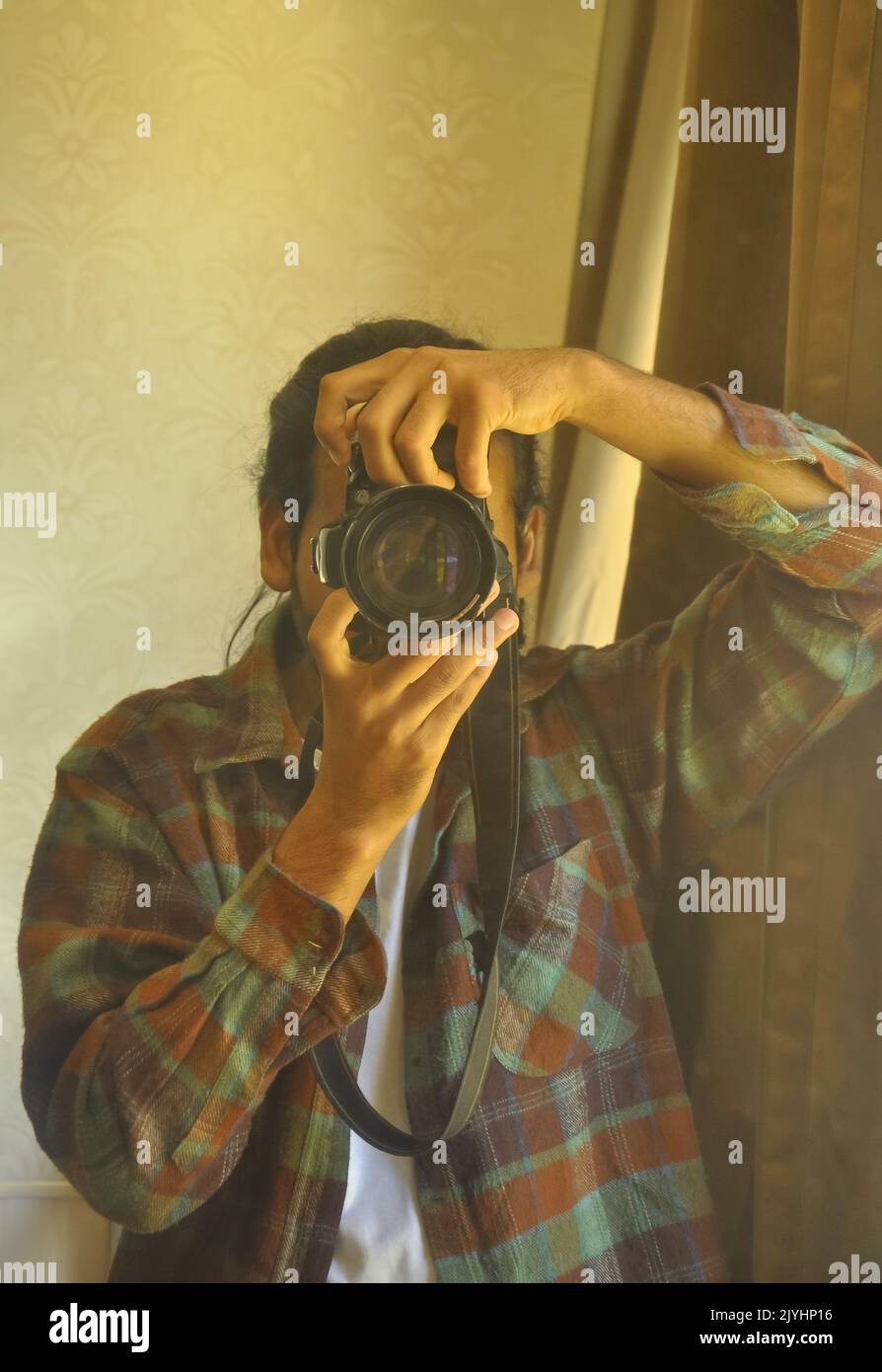 Die Taille eines männlichen Fotografen, der durch den Sucher seiner DSLR-Kamera schaut und vor dem Spiegel im Raum fotografiert. Stockfoto