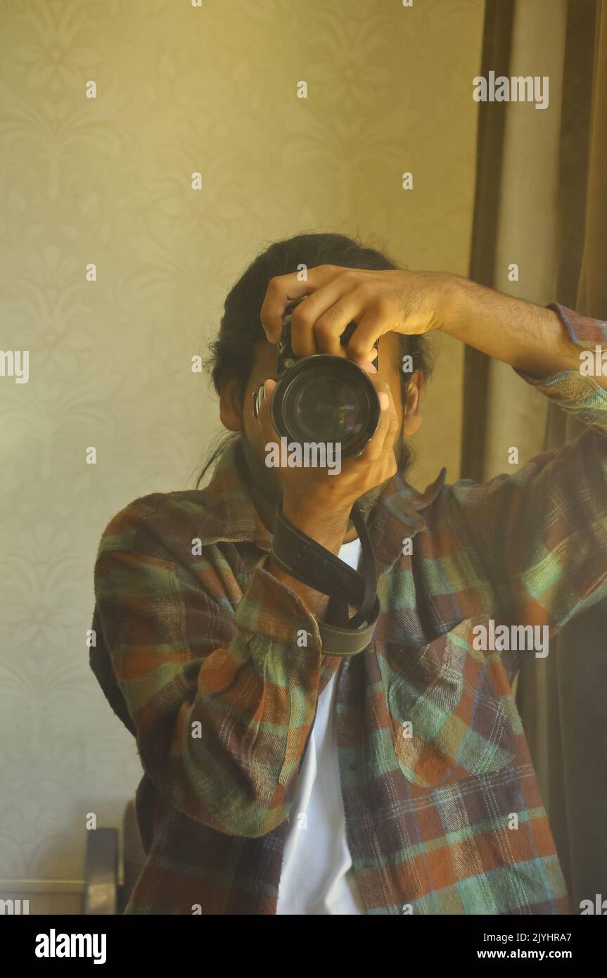 Die Taille eines männlichen Fotografen, der durch den Sucher seiner DSLR-Kamera schaut und vor dem Spiegel im Raum fotografiert. Stockfoto