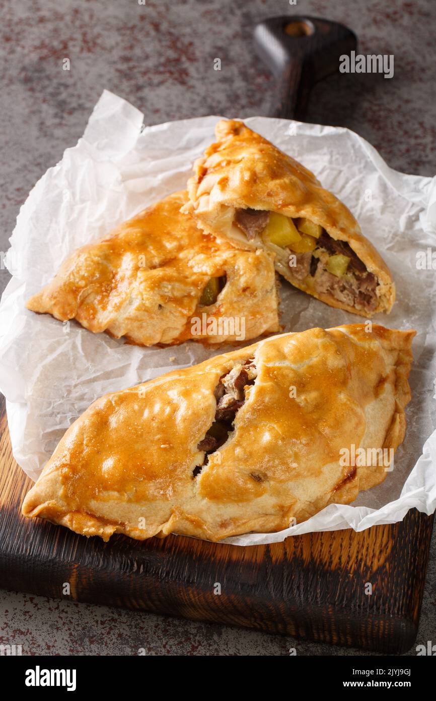 Frisch gebackene hausgemachte Cornish Pasties auf dem Papier auf dem Holzbrett. Vertikal Stockfoto