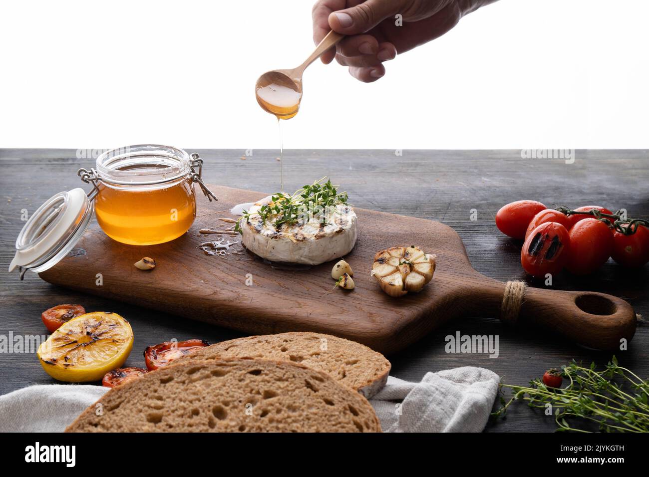 Der Camembert-Käse ist rund, gegrillt, mit goldenem Honig auf einem hölzernen Schneidebrett gegossen. Weicher selektiver Fokus, schwarzer Hintergrund.Platz zum Kopieren. Gesunde Ernährung. Stockfoto