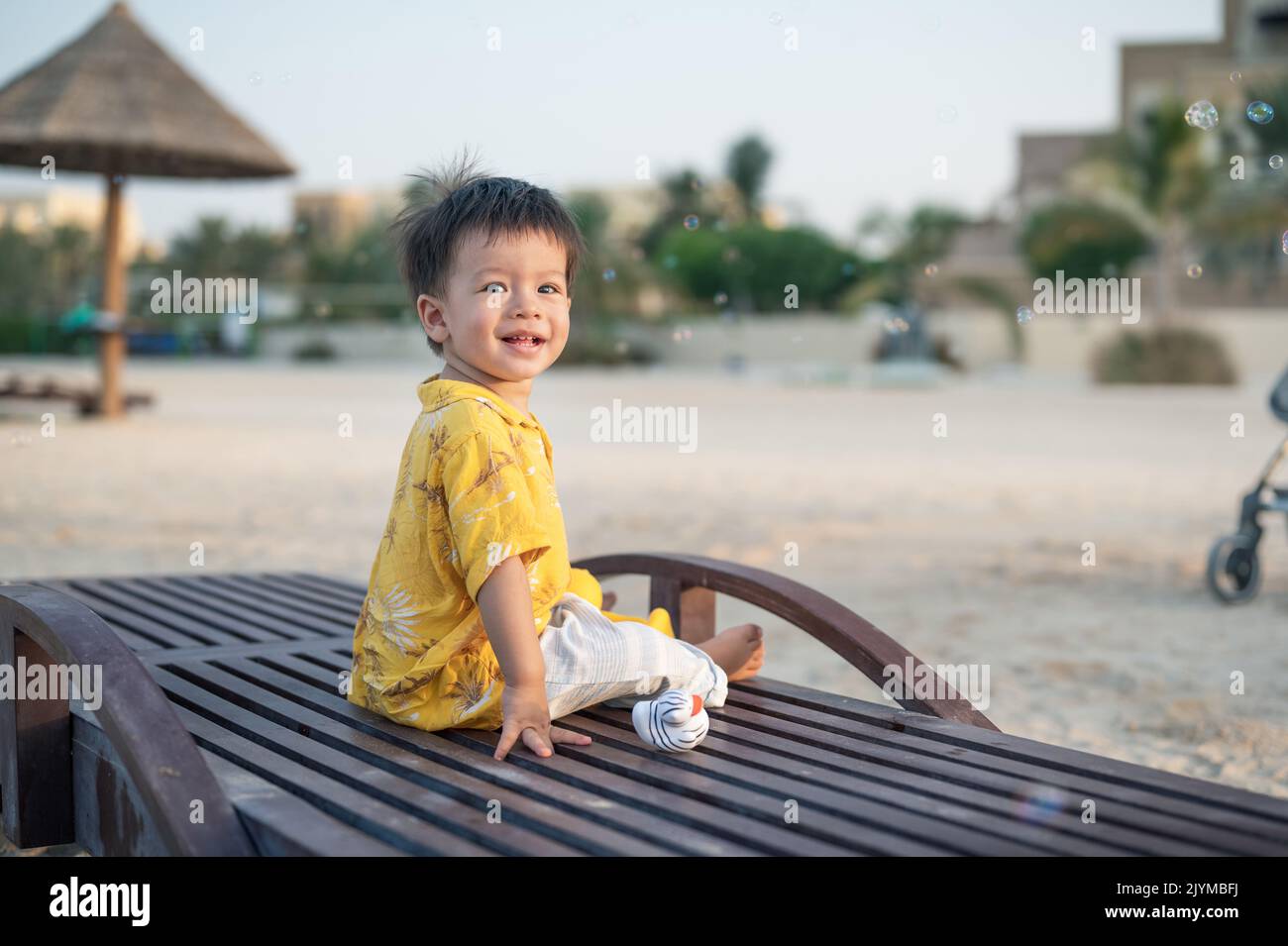 Kleiner Junge auf einem Strandurlaub, der bei Sonnenuntergang auf der Sonnenliege sitzt. Ein Jahr alter männlicher Säugling im Urlaub am Meer auf der Sonnenliege sitzen Stockfoto