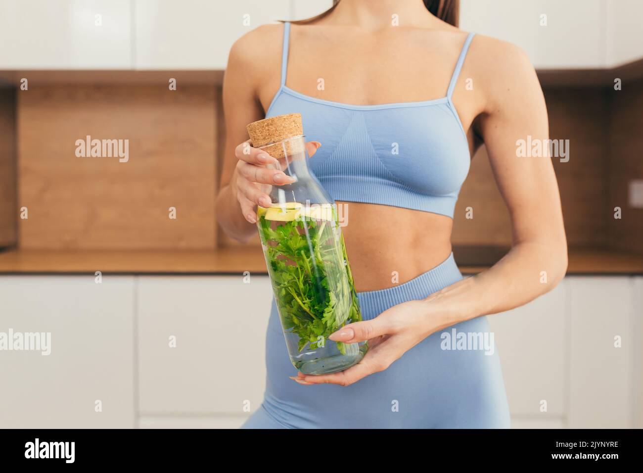 Nahaufnahme eines Körperteils einer jungen Fitness-Frau, die eine Flasche frischen Saft hält und zeigt und zu Hause entgiftet Stockfoto