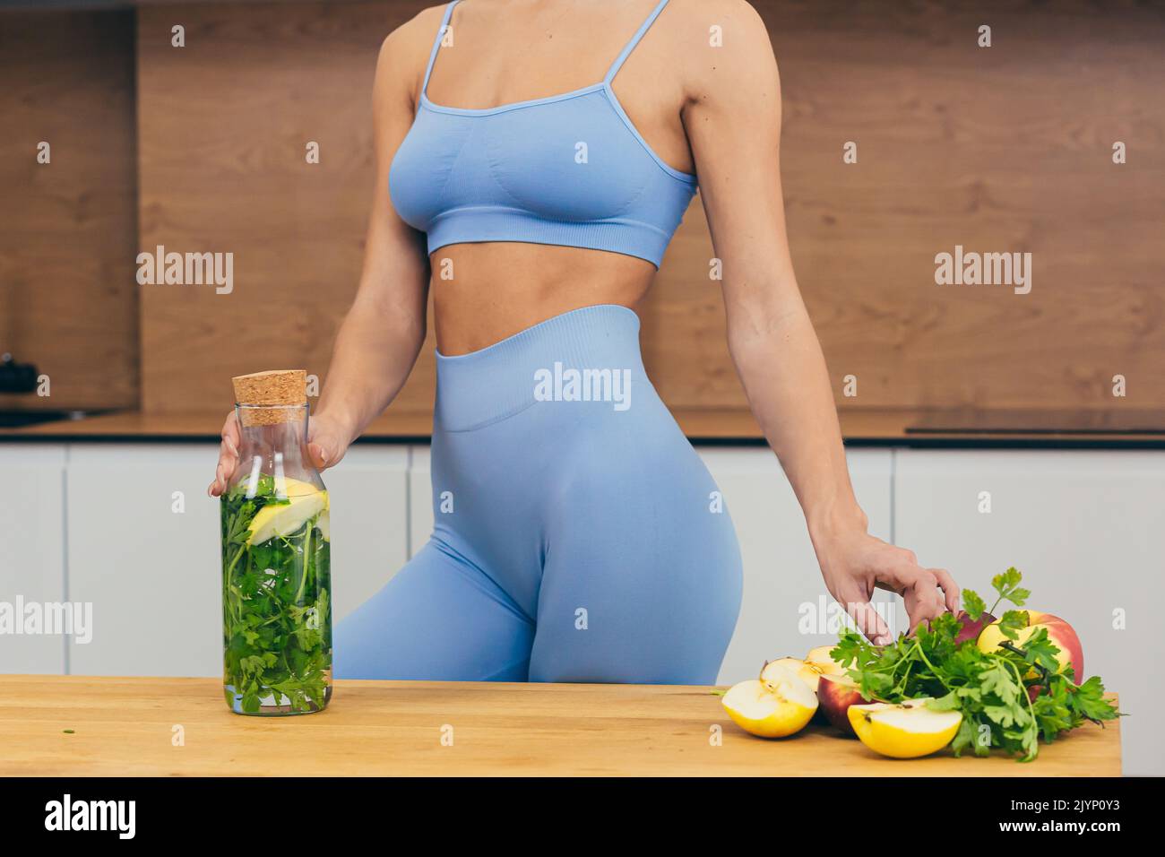 Nahaufnahme Foto Körper Teil der jungen Fitness-Frau stehend und hält Flasche mit frischem Saft, Entgiftung und frischem Gemüse zu Hause in der Küche Stockfoto