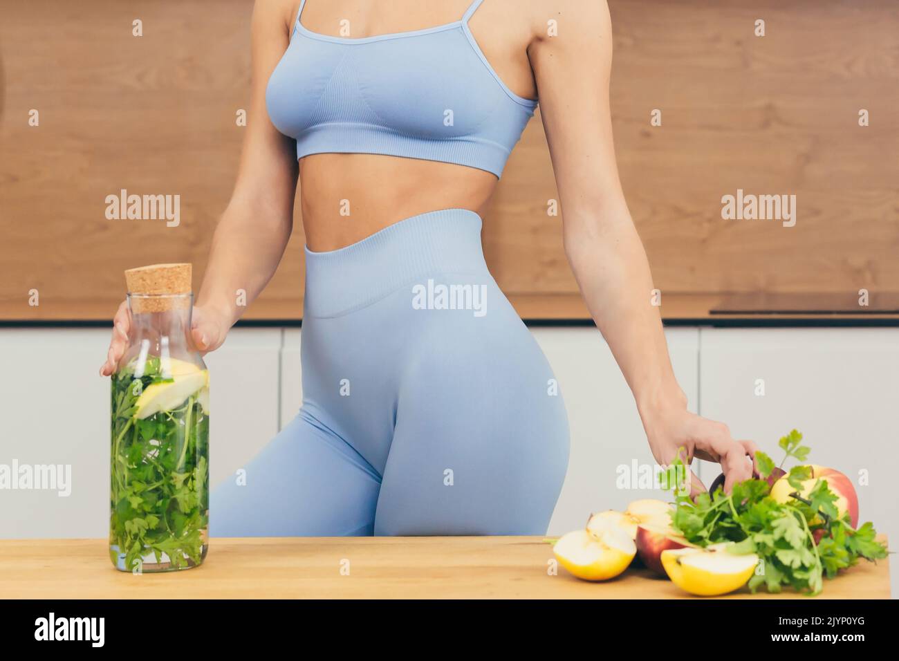 Nahaufnahme Foto Körper Teil der jungen Fitness-Frau stehend und hält Flasche mit frischem Saft, Entgiftung und frischem Gemüse zu Hause in der Küche Stockfoto
