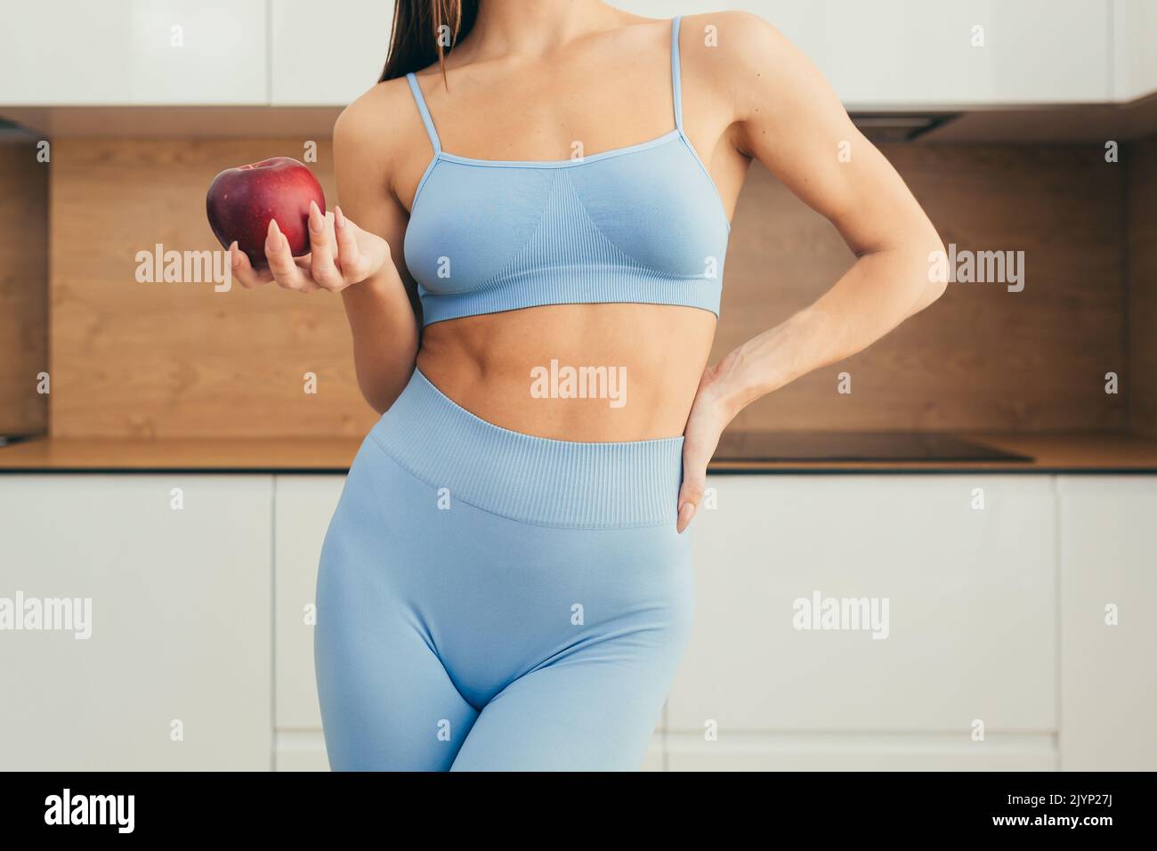 Nahaufnahme eines Körperteils, einer jungen Fitnessfrau, die zu Hause einen roten Apfel in der Hand hält Stockfoto