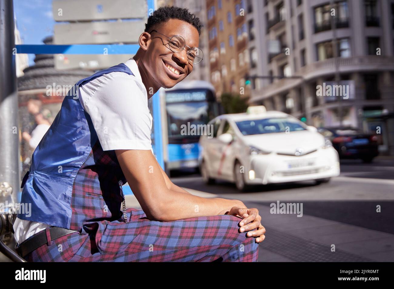 Junger afroamerikanischer Mann, der mit Einkaufstaschen an der Bushaltestelle sitzt. Stockfoto