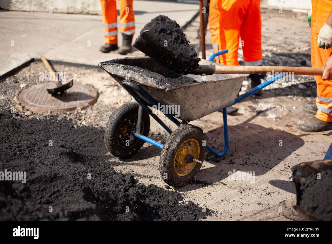 Reparatur der Straße. Asphalt auf der Straße verlegen. Arbeiter in orangefarbener Kleidung. Baumeister im Sommer in der Stadt. Stockfoto