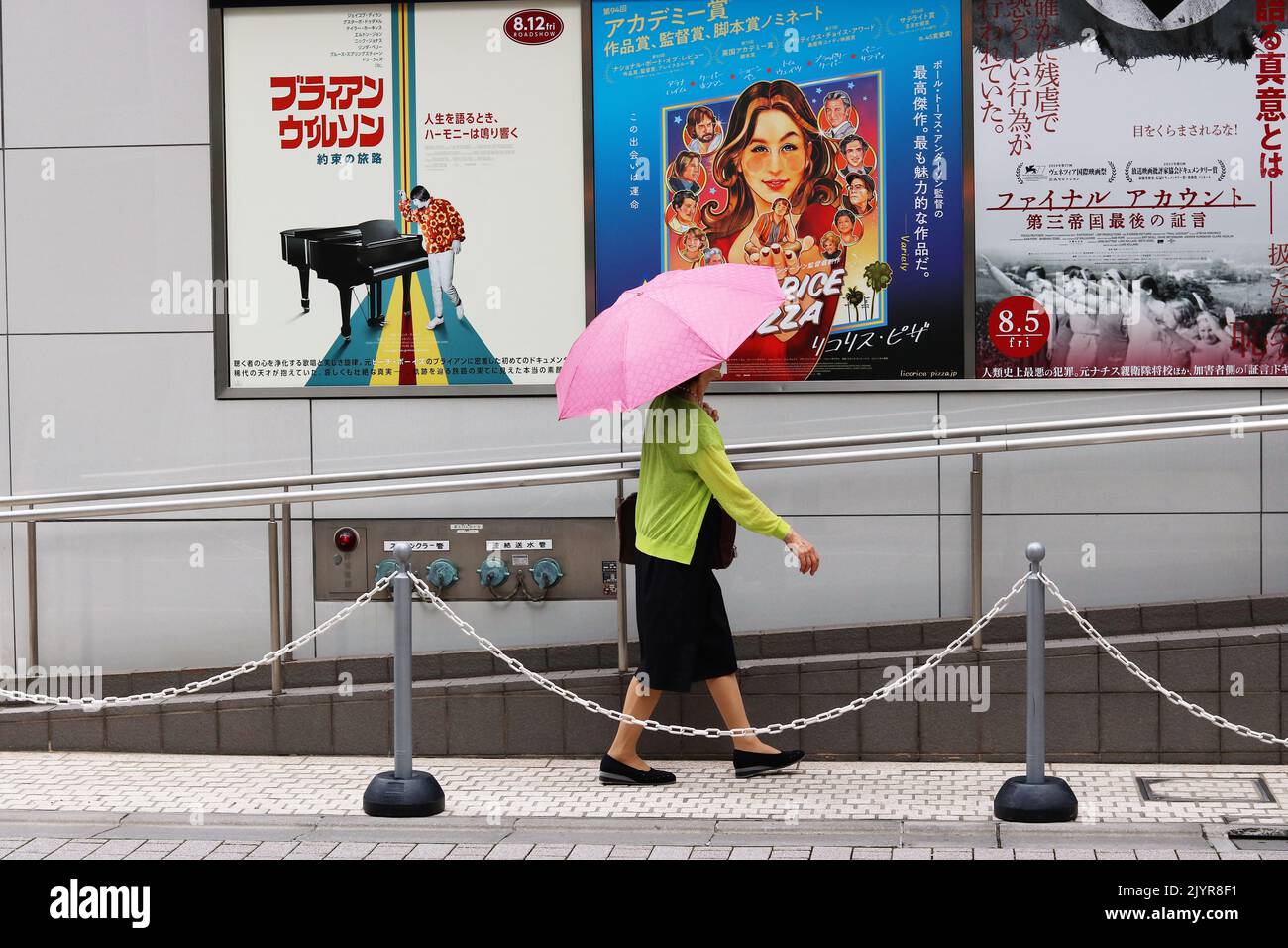 TOKIO, JAPAN - 1. September 2022: Ein Fußgänger mit einem Sonnenschirm passiert Filmplakate auf einem Toho-Kino in der Gegend von Tokio Hibiya. Stockfoto