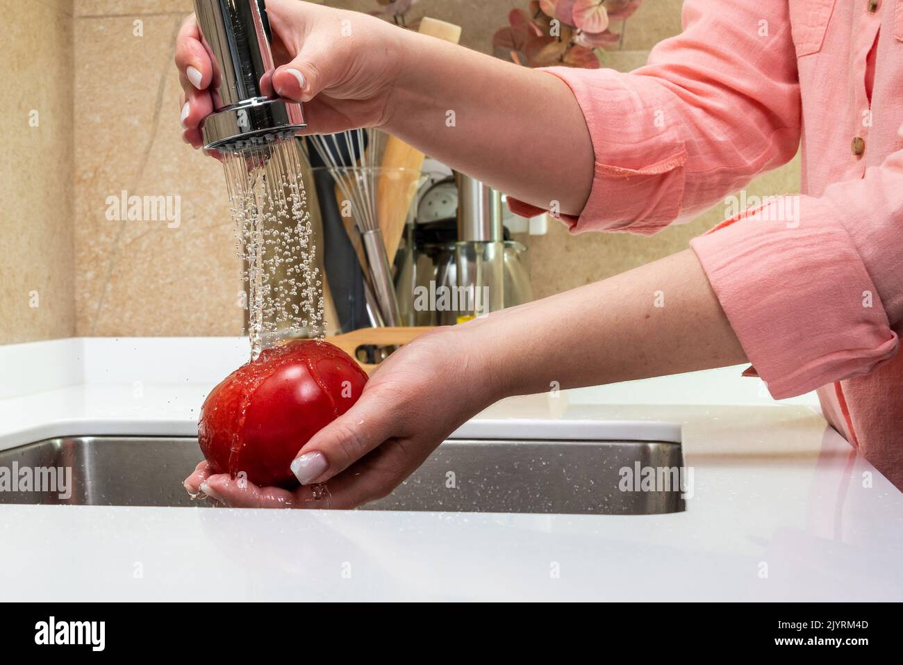 Seitenansicht der weiblichen Hände, die eine Tomate waschen Stockfoto