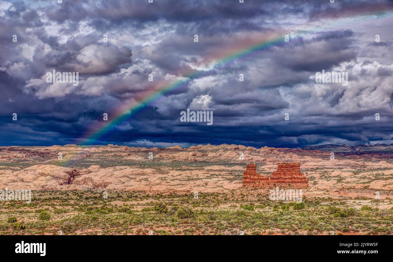 Ein Regenbogen über einem Sandsteinmonolith mit stürmischem Himmel über dem Arches National Park, Moab, Utah. Stockfoto