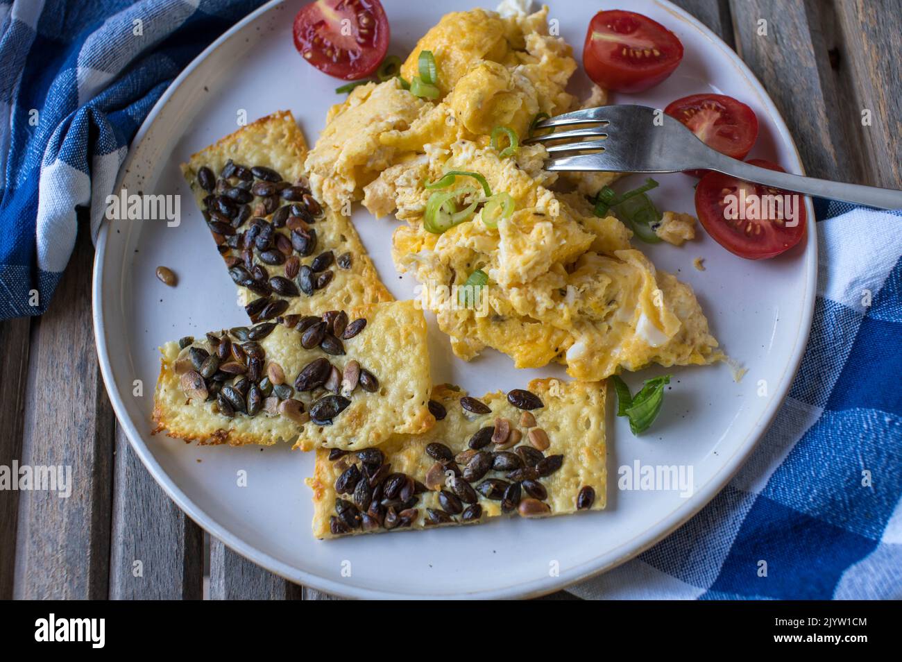 Ketogenisches Frühstück mit Rührei, Käse, Kürbiskern-Cracker und Tomaten Stockfoto