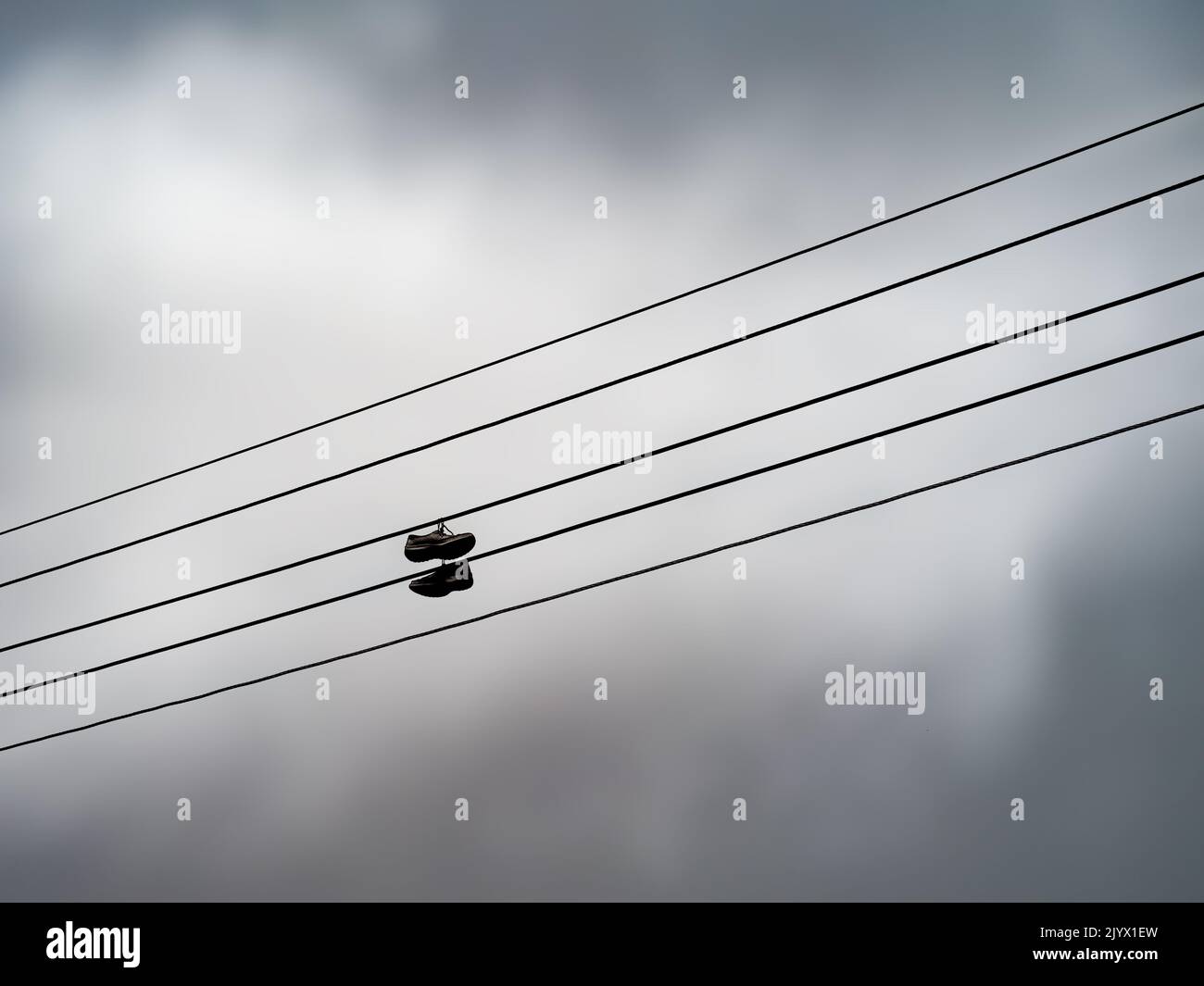 Nicht identifizierbare alte Sportschuhe, Schuhe über Telefonkabel. Stockfoto