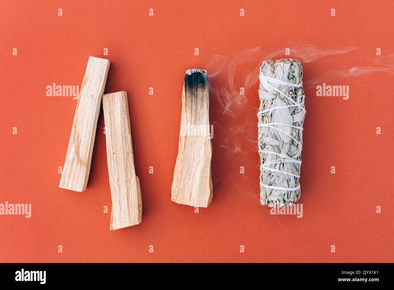 Schwelender Weihrauch. Weißer Salbei und palo santo stecken in einer Reihe auf orangerotem Hintergrund. Bundle für Meditation und Raumbegasung. Selektiver Fokus. Stockfoto