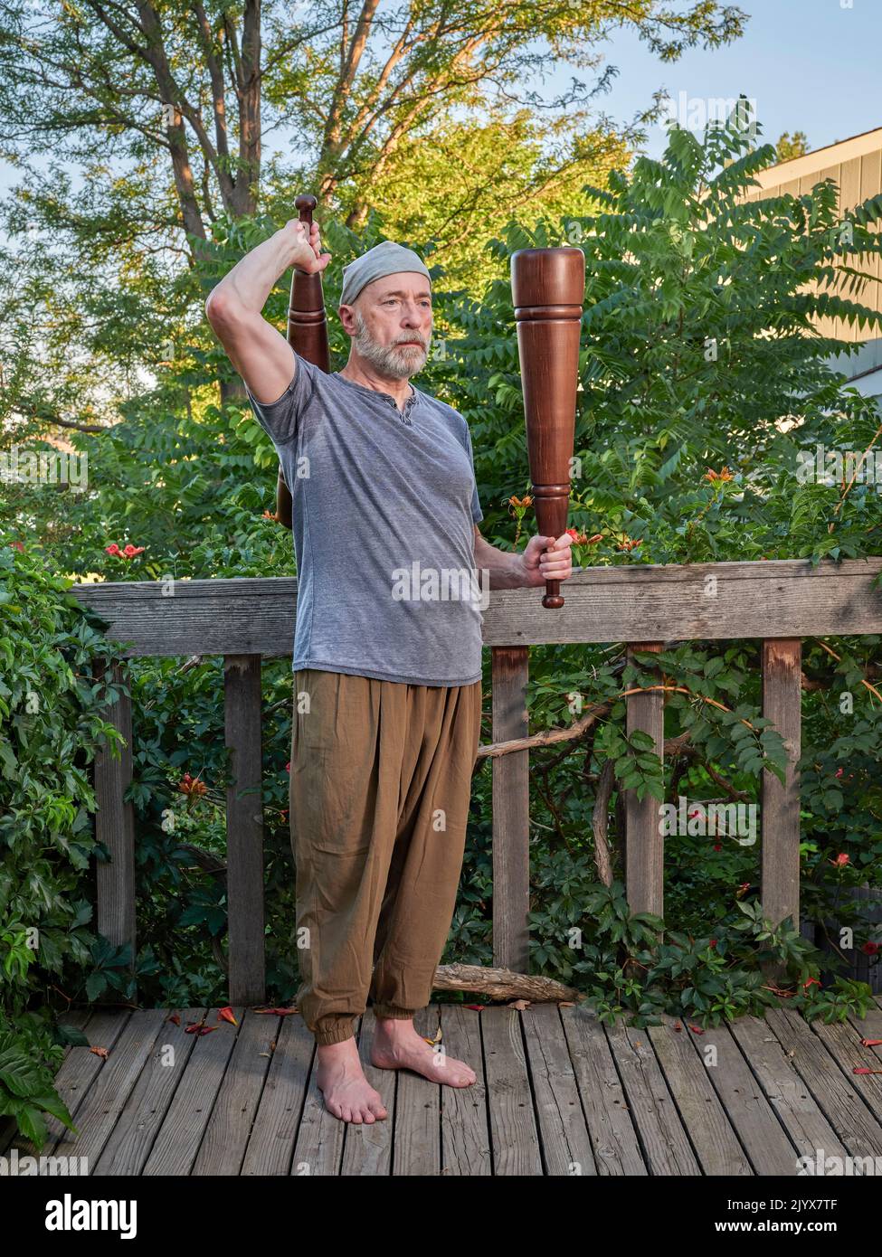 Der ältere Mann (Ende 60s) trainiert mit schweren persischen Meels auf seiner Hinterhofterrasse, funktionelles Fitnesskonzept mit traditionellen Werkzeugen Stockfoto