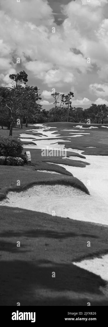 Die lange Sandfalle zieht sich durch dieses starke vertikale Panoramabild. Blauer Himmel mit Wolken. Gepflegtes Gras kantet die schwierige Sandfalle. Stockfoto