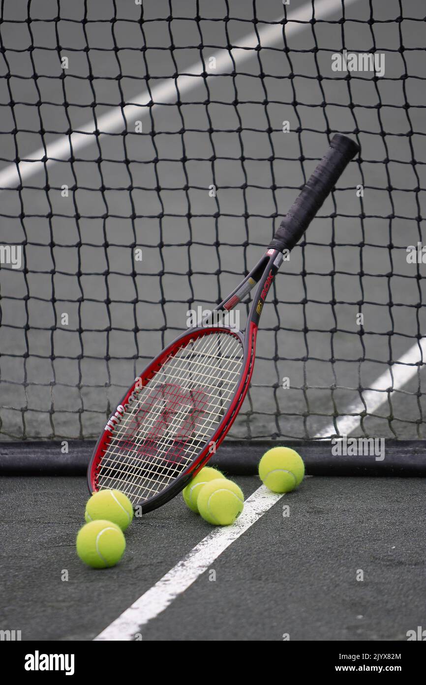 Tennisschläger, der sich gegen das Netz lehnt, mit Tennisbällen auf dem Platz. Gelbe Tennisbälle auf dem Platz in der Nähe einer Foul Line. Stockfoto