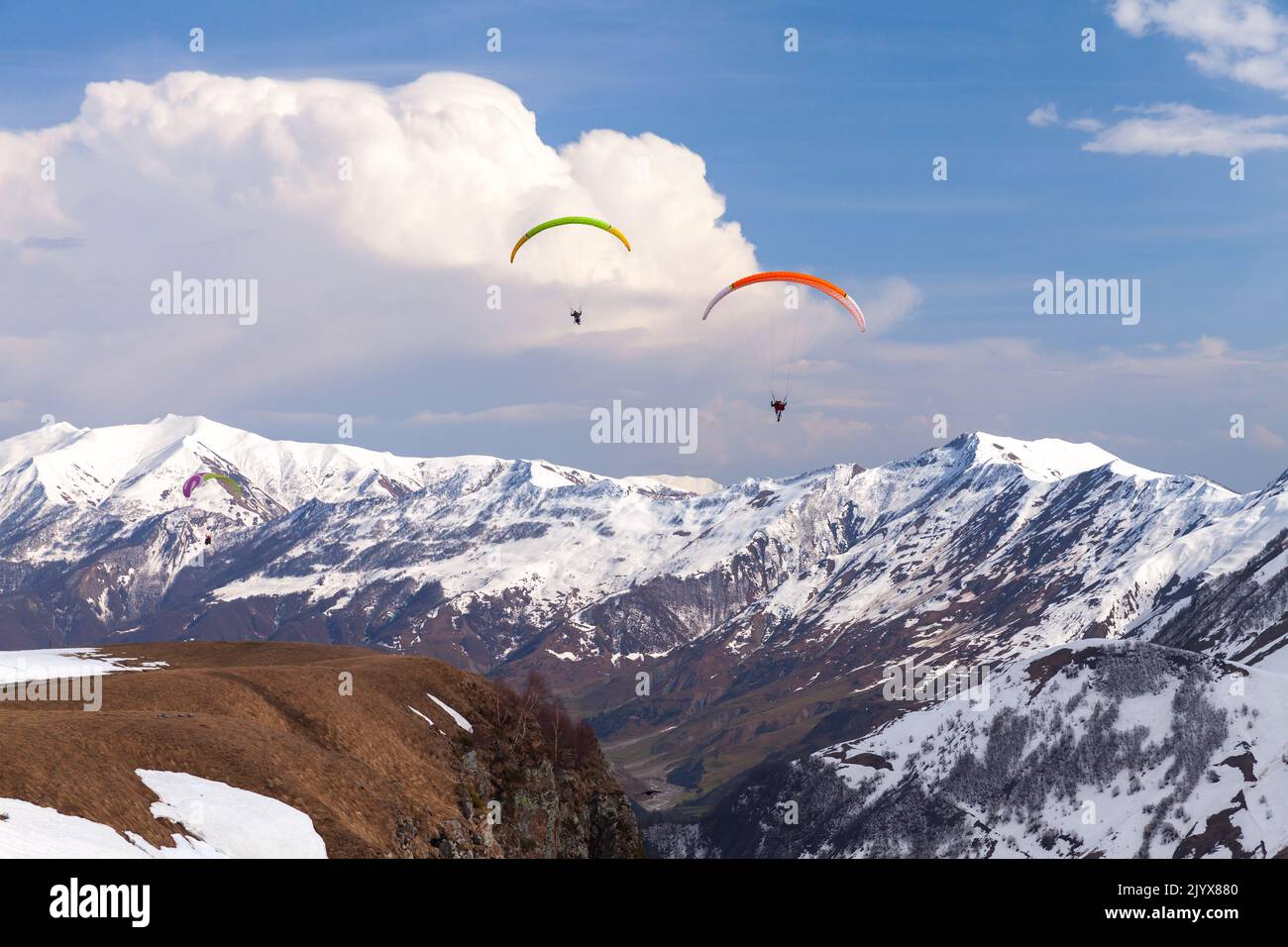 Berglandschaft mit Gleitschirmen, die tagsüber in der Nähe von verschneiten Gipfeln des Kaukasus fliegen. Gudauri, Georgia Stockfoto