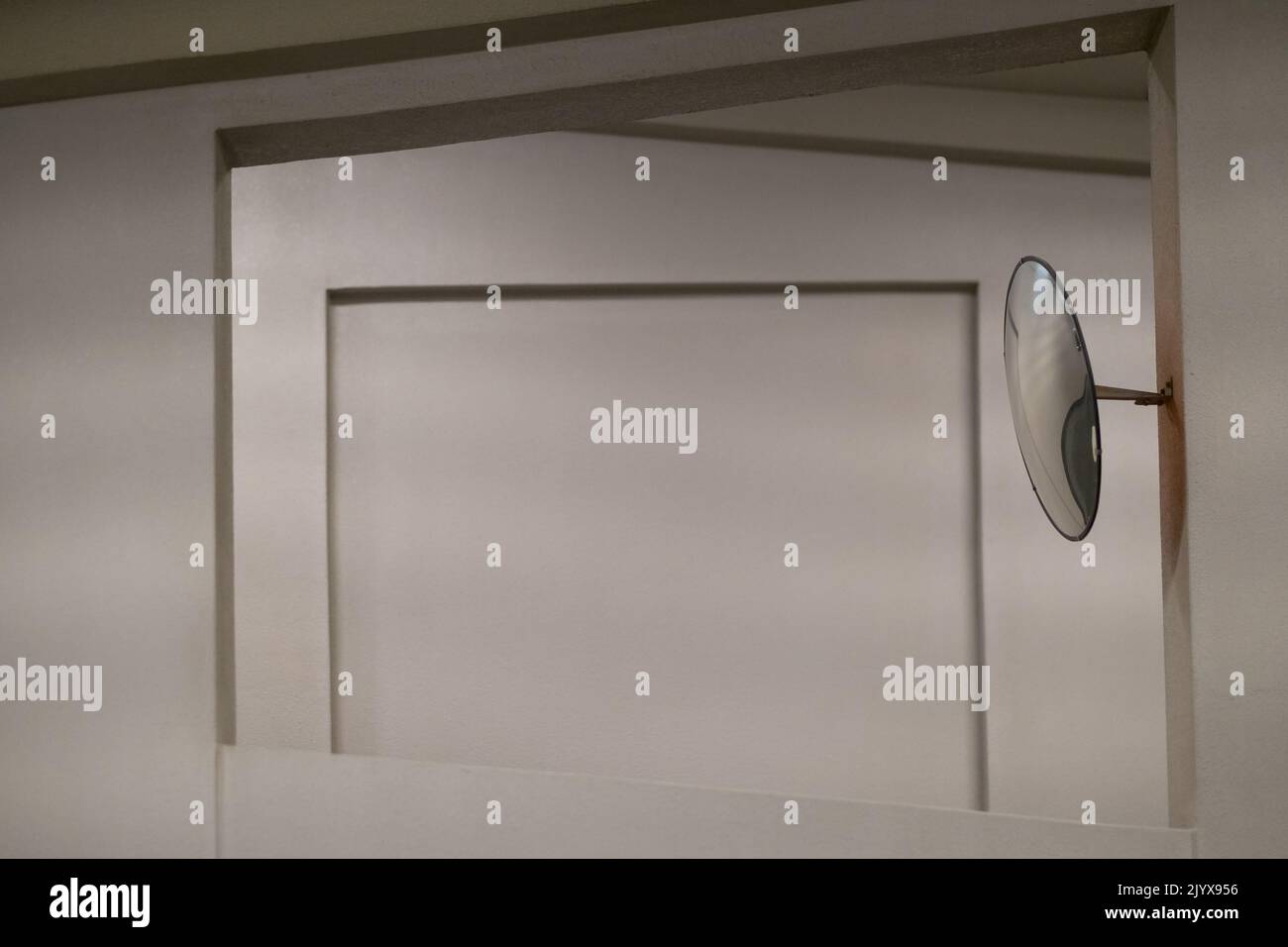 Großer runder Spiegel, der in eine Wand gebohrt wurde, die zwei Rampen in einem mehrstöckigen Parkplatz trennt. Konvexes Glas dient der Sicherheit. Das Element wird von einem Fenster eingerahmt. Stockfoto