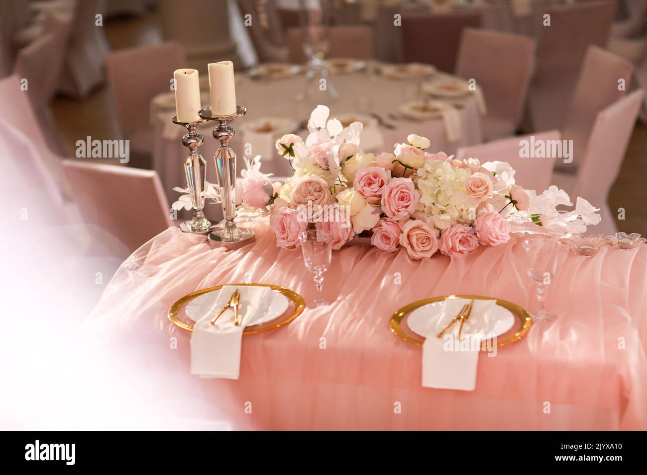 Tischdekoration mit rosa Tischdecke, Kristall Kerzenleuchter mit Kerzen und weißen rosa Blumen im Restaurant. Stilvoller Hochzeitstag Stockfoto