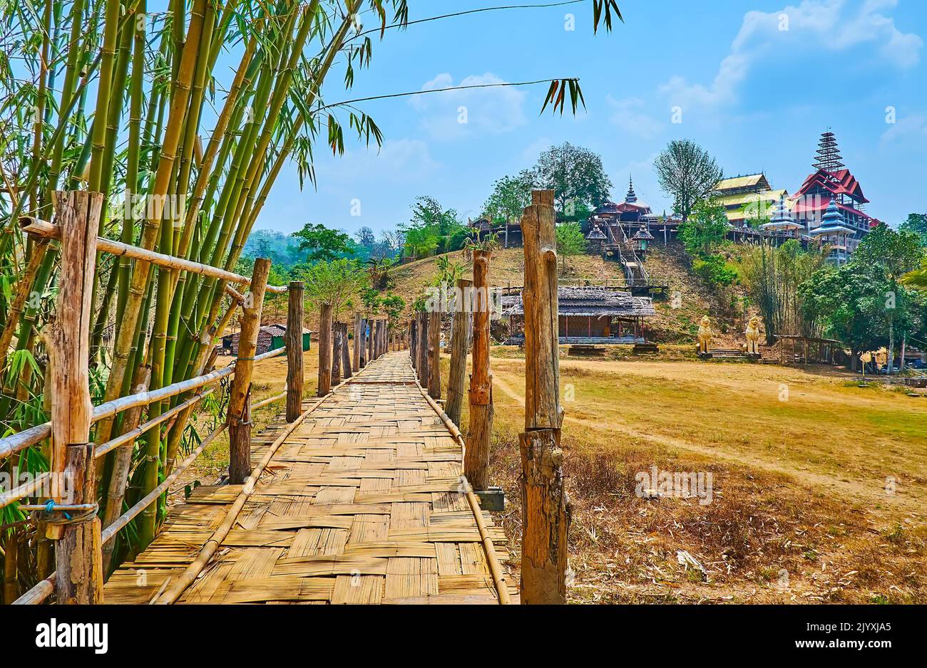 Die alte Shabby Su Tong Pae Bamboo Bridge in hügeliger Landschaft mit dem Wat Tham Poo Sa Ma buddhistischen Tempel auf dem Hügel im Hintergrund, Mae Hong Son subu Stockfoto