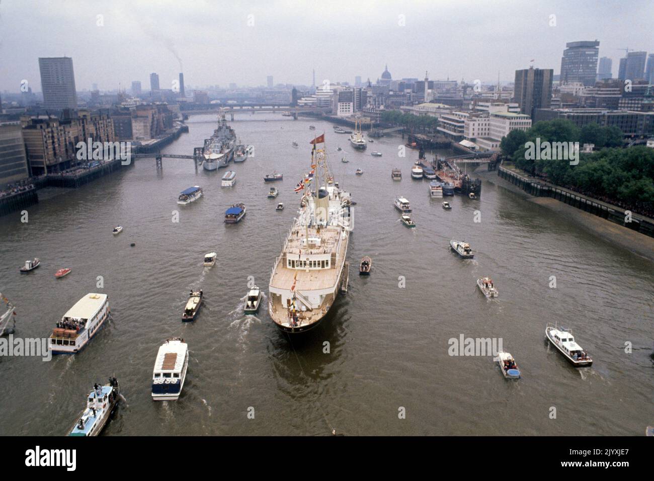 Datei-Foto vom 9/6/1977 von einer Flottille kleiner Schiffe rund um die Royal Yacht Britannia im Pool von London, als die Queen während ihres Flußfortschritts von Greenwich nach Lambeth eine Mittagsfeier an Bord gab. Im Hintergrund ist die HMS Belfast mit der Minensuchboot HMS Croften. Beim Silberjubiläum der Königin von 1977 feierten Millionen ihre Herrschaft auf Straßenfesten im ganzen Land, und die Zuneigung, die die Menge zeigte, war sogar für die Königin eine Überraschung. Ausgabedatum: Donnerstag, 8. September 2022. Stockfoto