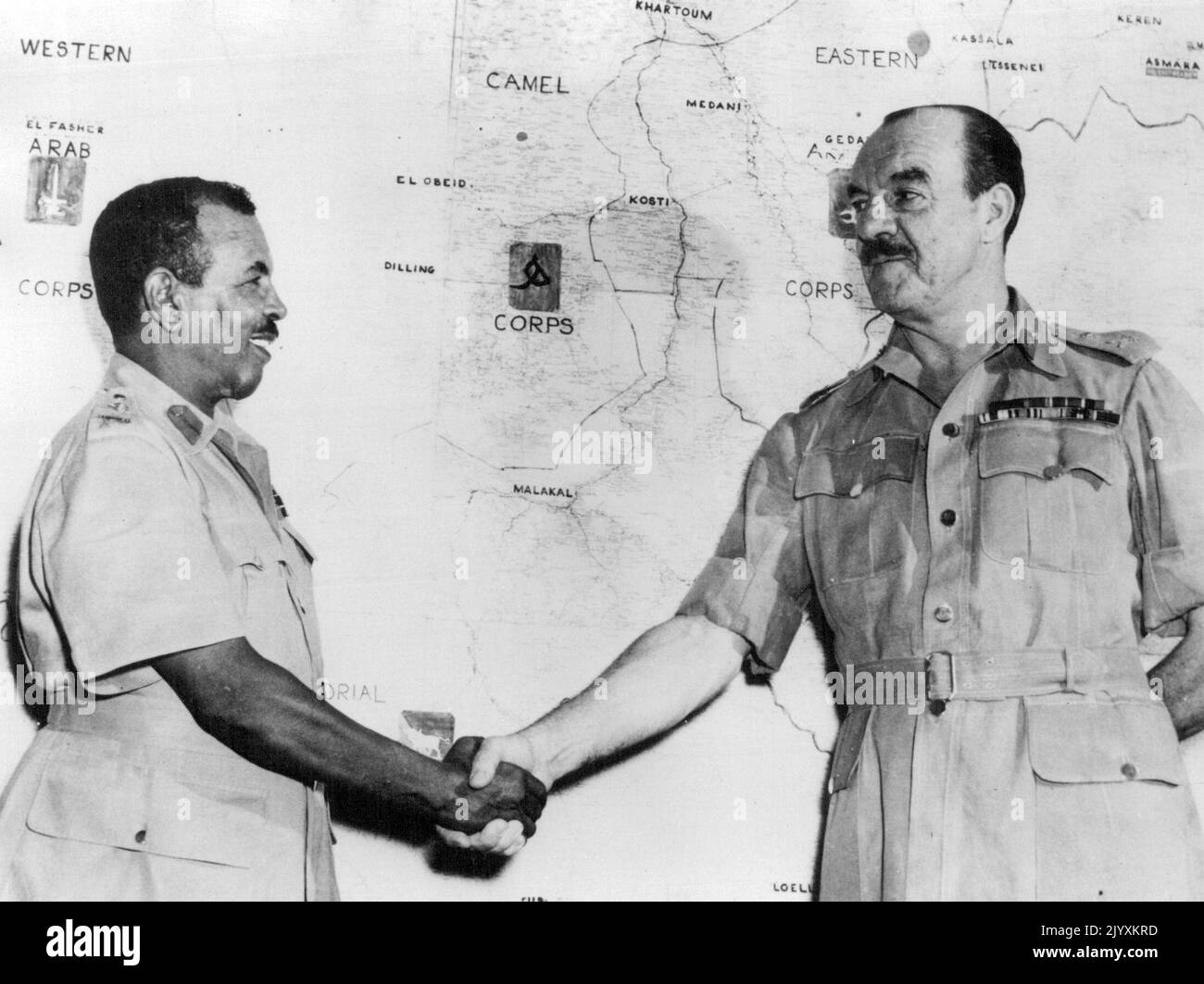 Britischer General fliegt aus dem Sudan -- Major-General R.L. Scoones, C.B., D. S. O., O. B. E., verabschiedet sich von seinem stellvertretenden Kommandanten, Brigadier Ahmed Pasha Mohammed, O. B. E., der das Kommando übernimmt. Die Änderung erfolgt im Rahmen der Politik der "Sudanisierung" der militärischen Kontrolle im Sudan. General Scoones flog mit dem Flugzeug der RAF vom Flughafen Khartum nach Großbritannien zurück. Im Hintergrund ist eine Karte mit dem Provinzhauptquartier des Sudan Defence Force Corps zu sehen. 17. August 1954. (Foto von United Press Photo). Stockfoto